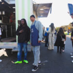 Two men standing near a truck, one wearing bright neon green shoes.