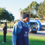 Volunteers in aprons assisting at an outdoor event near a park with tents and vehicles.