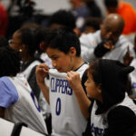 A woman wipes tears holding a Clippers jersey in a crowded room.