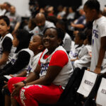 A smiling woman in red sportswear among seated children at an event.