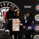 Three people holding a certificate on stage at an event with a black backdrop.