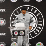 A man in a gray jacket speaking at a Clippers podium.