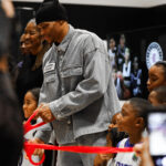 Man cutting a red ribbon at a public event with excited children nearby.