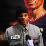 Man in denim jacket and beanie speaking to reporters.