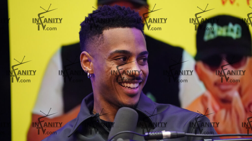 A smiling man speaking into a microphone at an event.