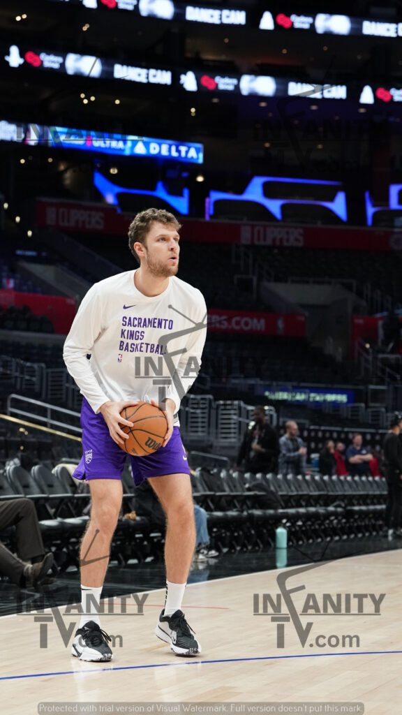 Basketball player in white shirt and purple shorts holding a ball on court.
