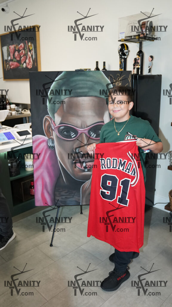 Young boy holding a red basketball jersey in front of a colorful mural.