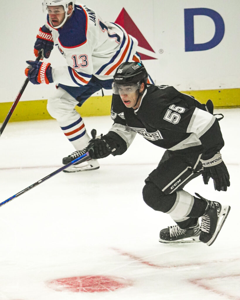 Ice hockey player in black uniform skating with puck during a game.