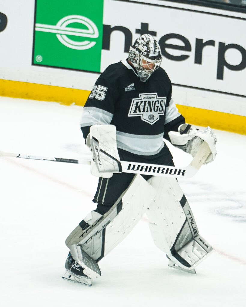 Hockey goalie in black and white Kings uniform ready in net.