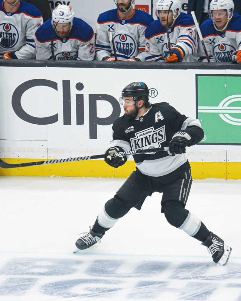 Hockey player in black Kings uniform skating on ice during a game.