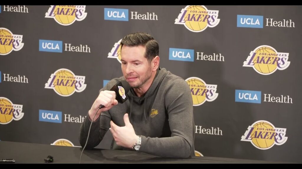 A man speaking at a Lakers press conference with a microphone.