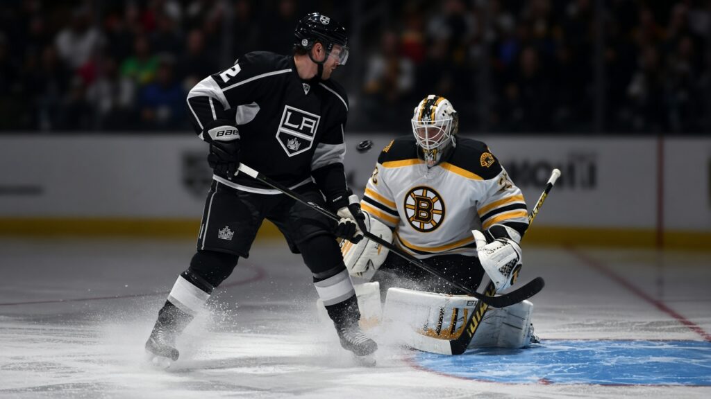 A Kings forward in a black jersey screens a Boston Bruins goalie in white as a point shot comes in