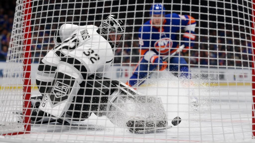 A Kings goalie in white makes a pad save seen through the net mesh against the Islanders