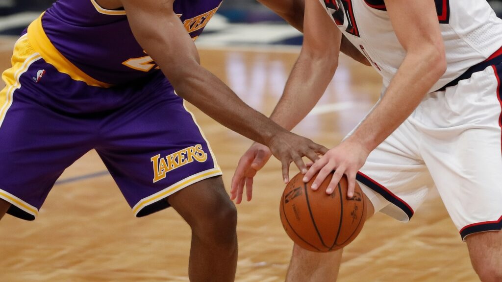 Close-up of a defender in a purple and gold LAKERS uniform poking the basketball loose from a dribbler's hand on the hardwood.
